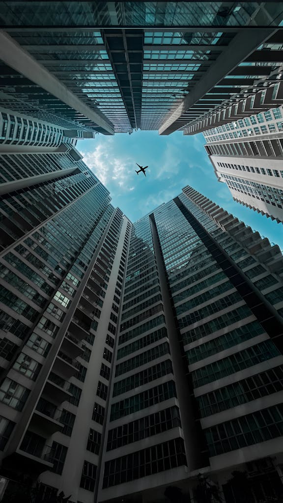 Dramatic view of modern skyscrapers forming a canyon with airplane overhead.